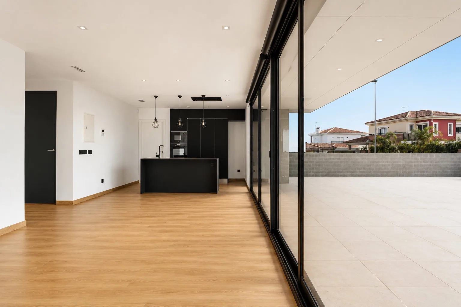Salón-cocina diáfano de la Homi II con isla en negro mate y suelo de madera abierto a la terraza